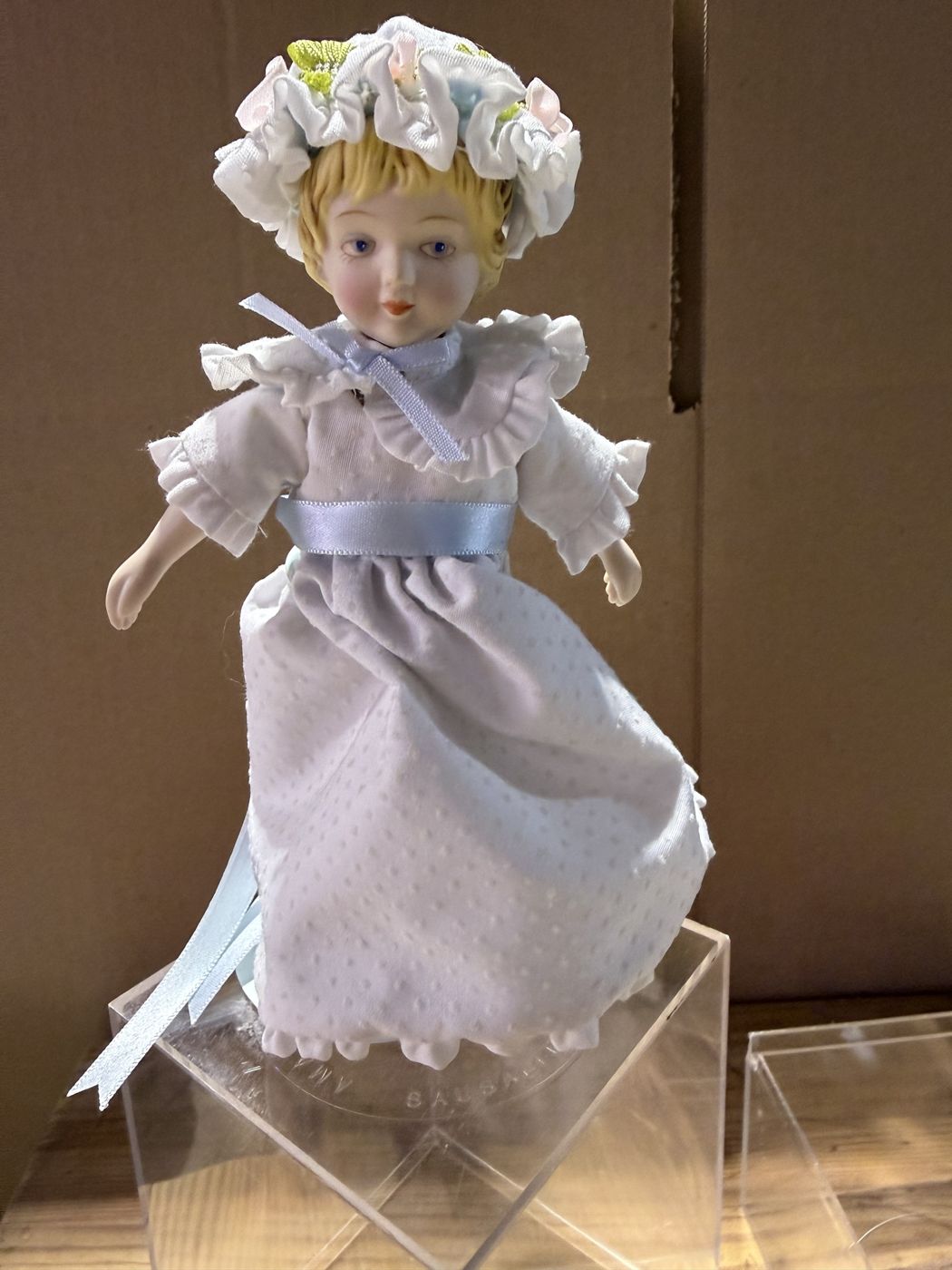 Bisque doll in a white dotted swiss dress on an acrylic case