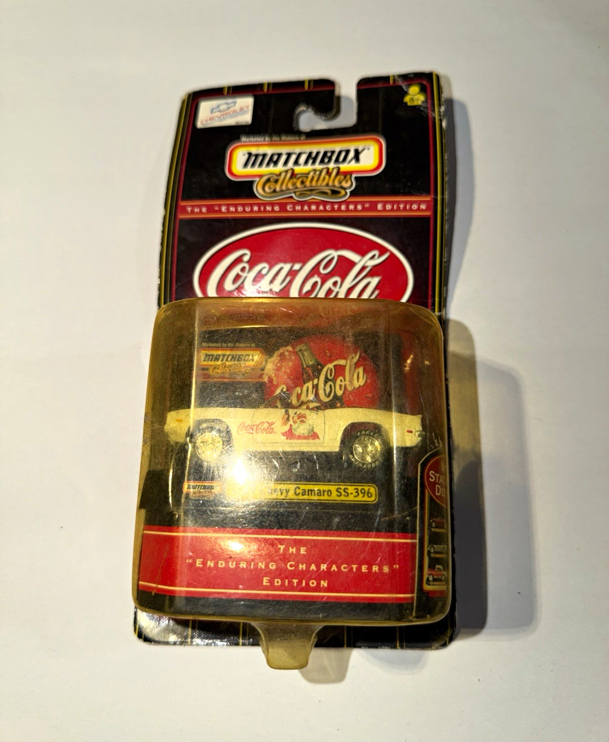 A dusty, scuffed blister card holding a Matchbox Coca-Cola Camaro, photographed as found